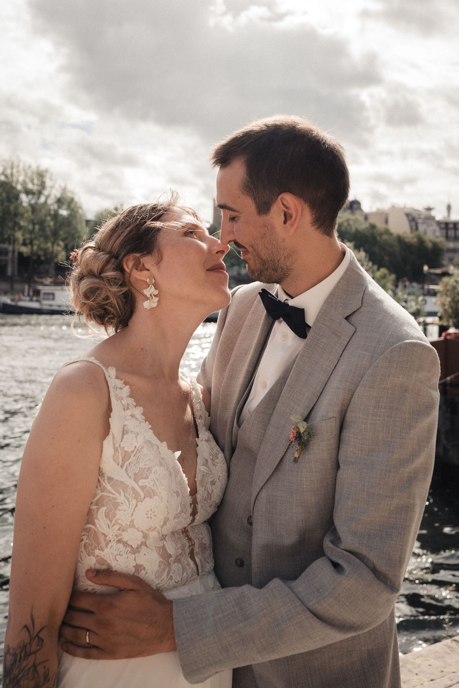 Romantic wedding couple shares intimate moments by the water during sunset photo session in grey and white attire.