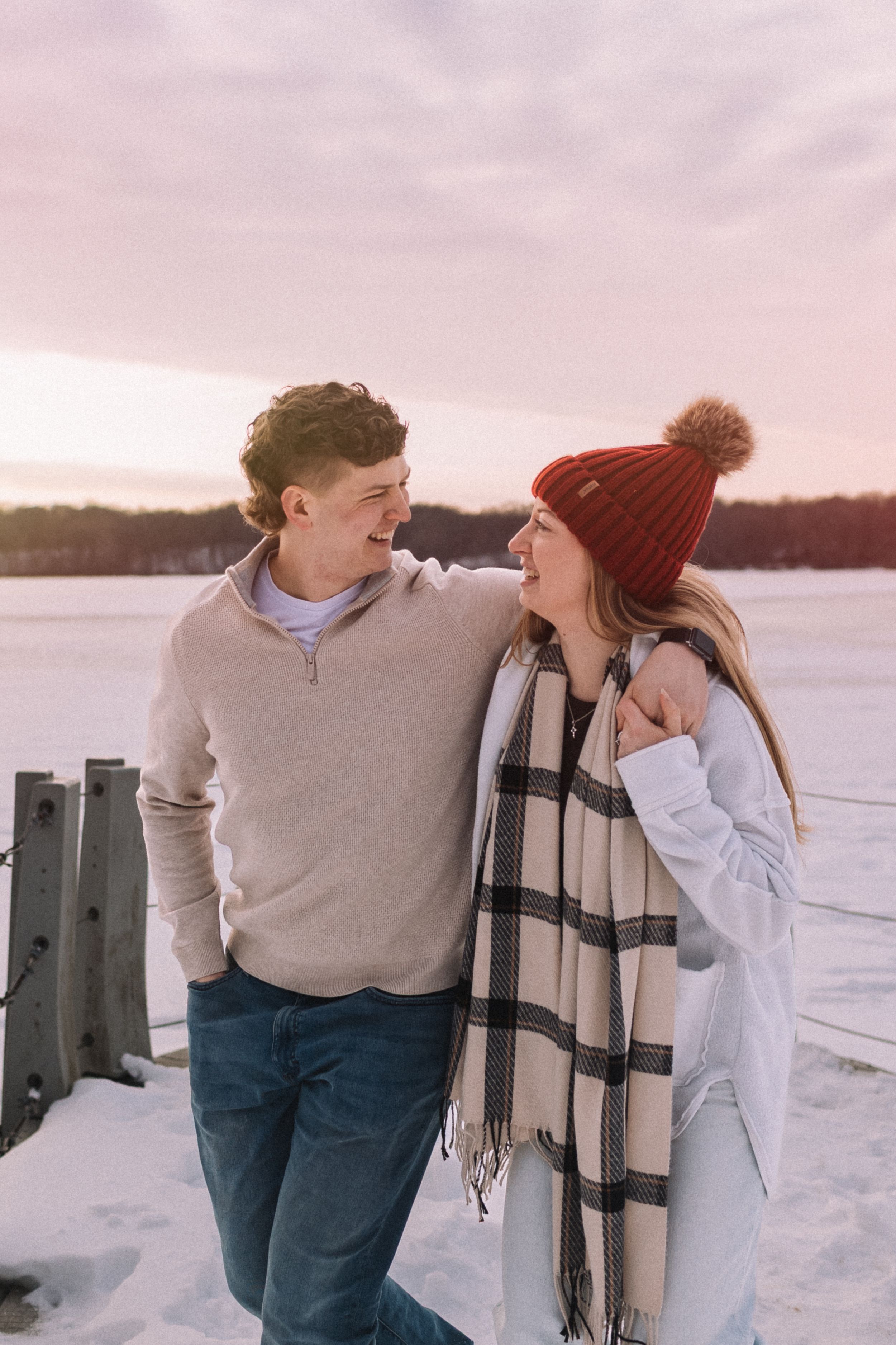 A couple shares tender moments on a snowy winter day by a frozen lake while wearing cozy winter attire.