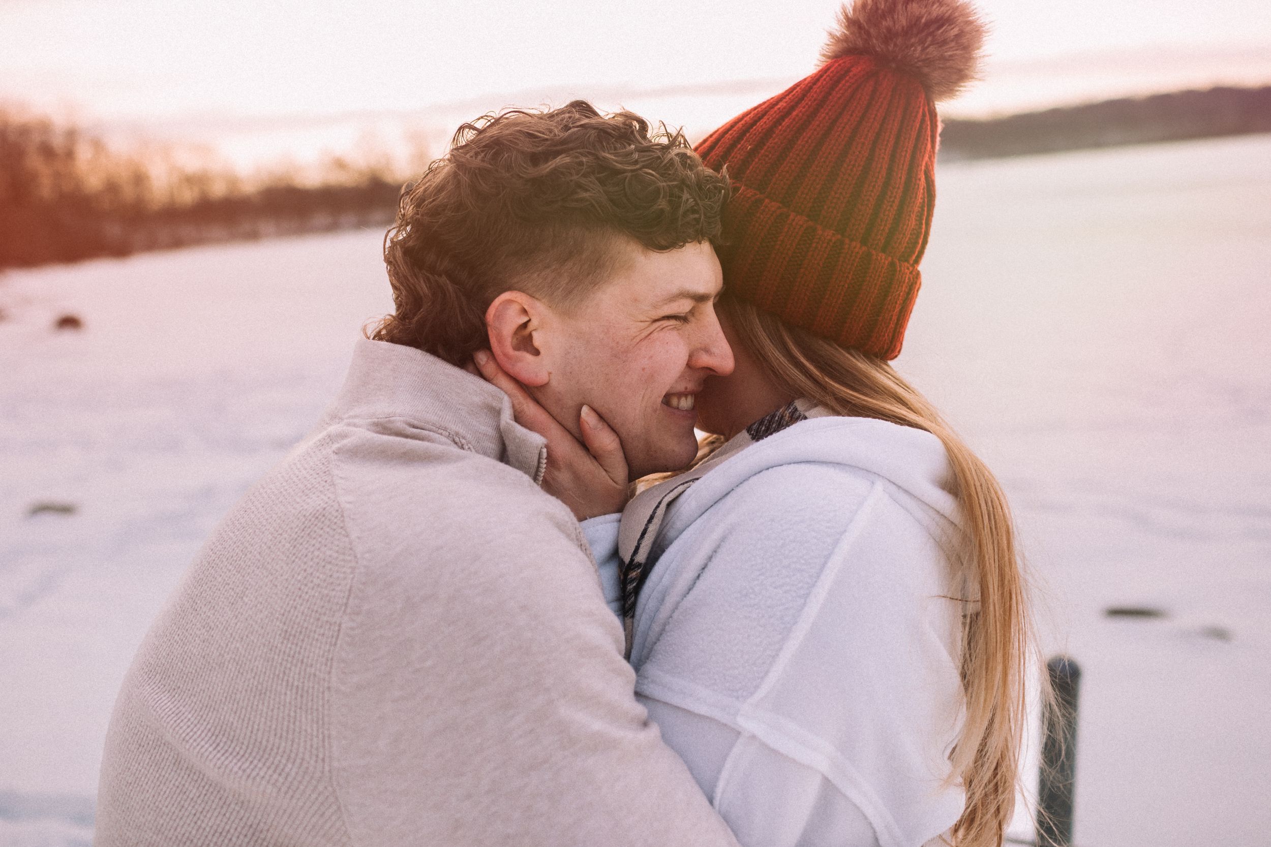 A couple embraces and shares a romantic moment in the snowy winter landscape during sunset.