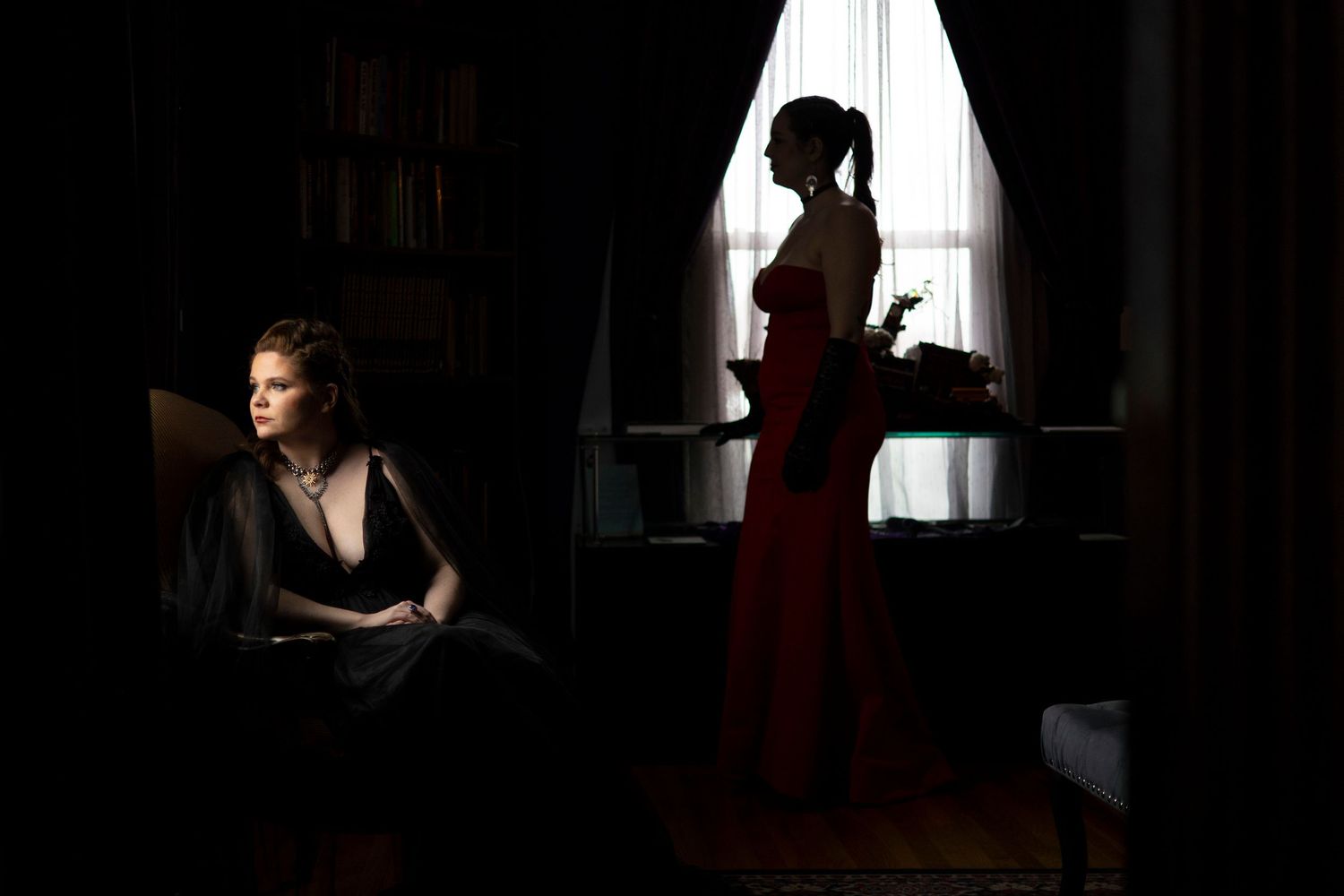 Dramatic noir-style photo of a woman in a black alternative wedding gown looking out of a window in a library in Salem.