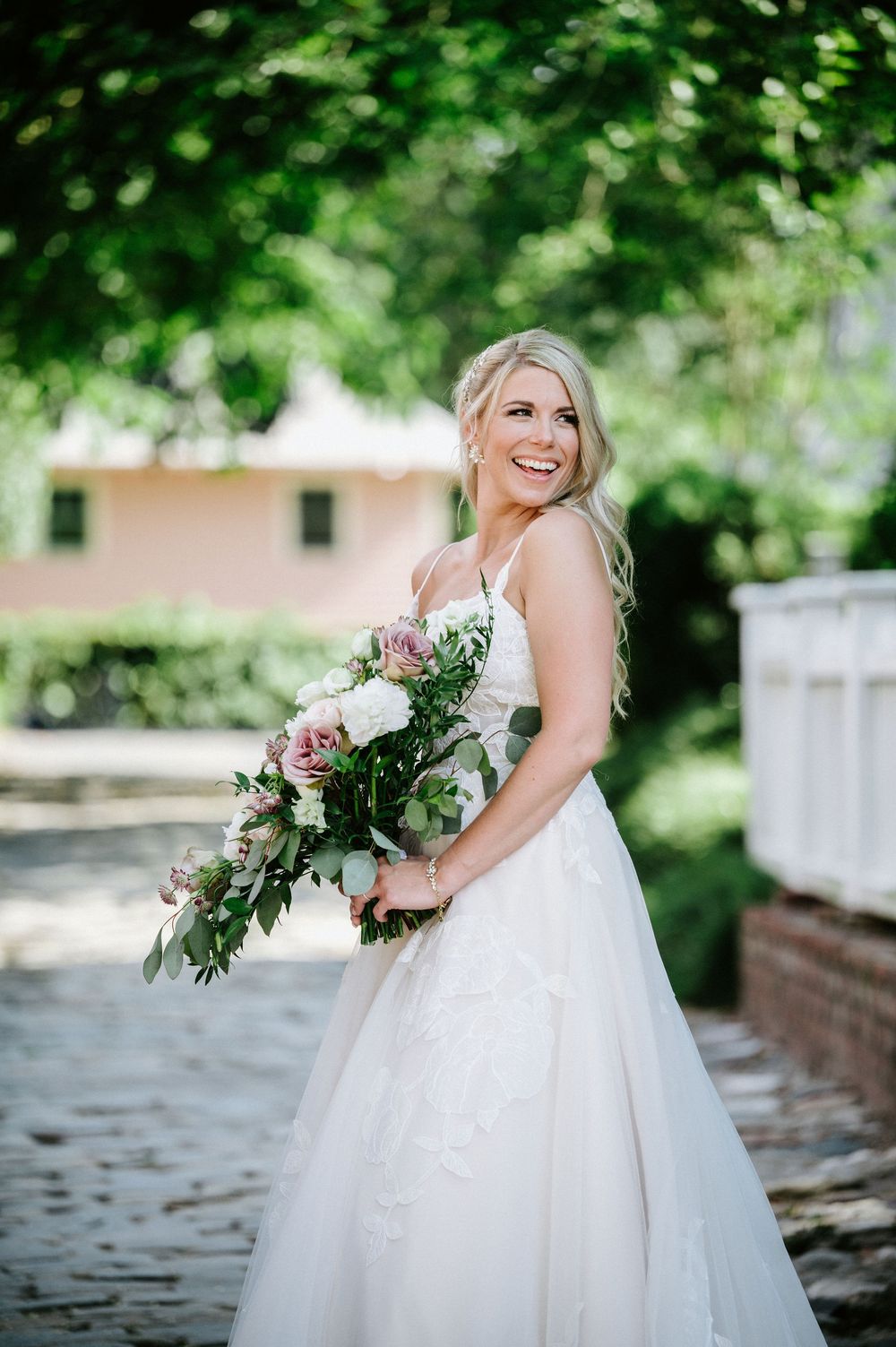 A bride in a flowing white gown poses with a lush bouquet in an outdoor garden setting.