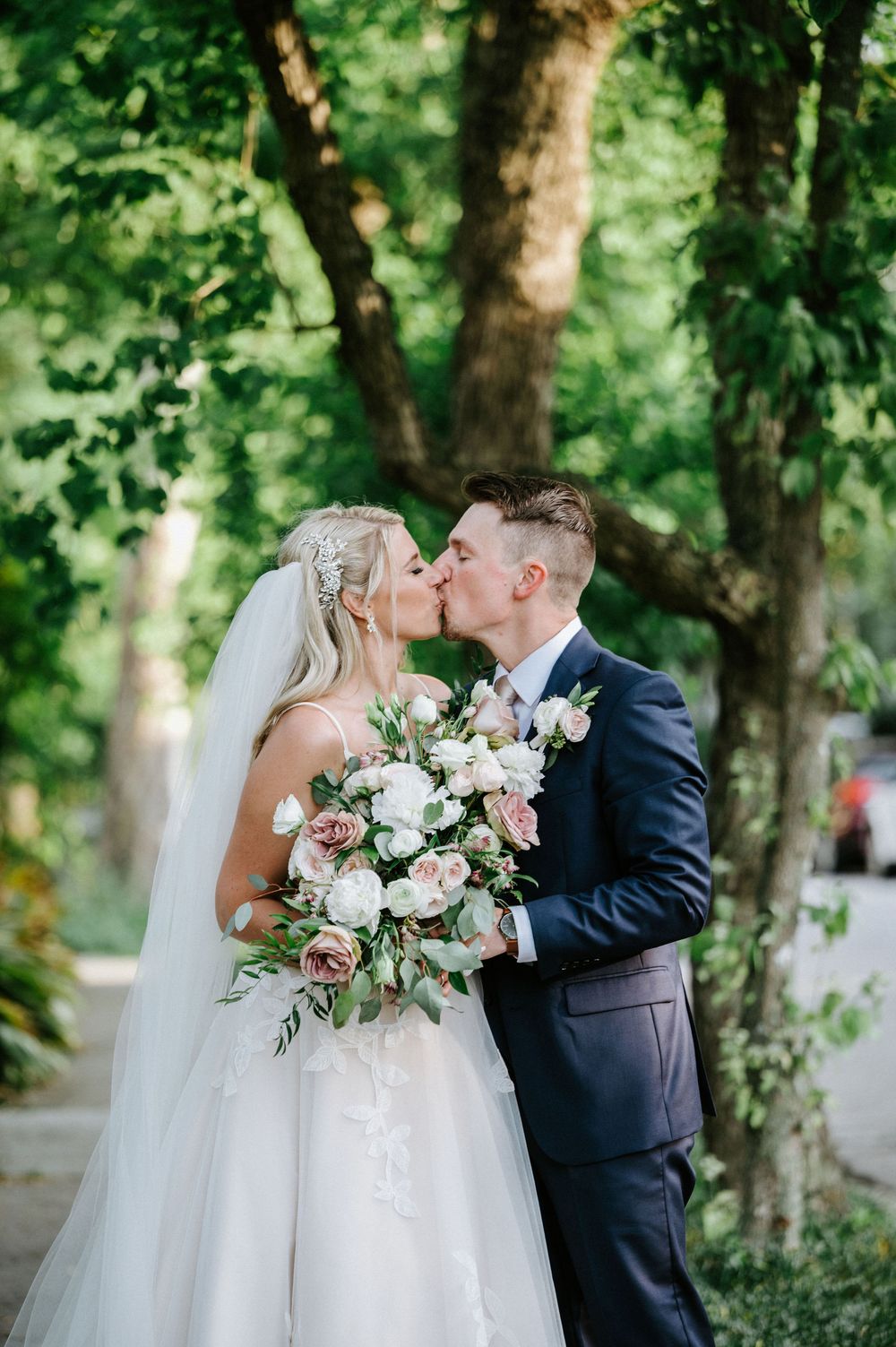 A romantic wedding couple shares intimate moments in a lush garden setting with a beautiful white floral bouquet.