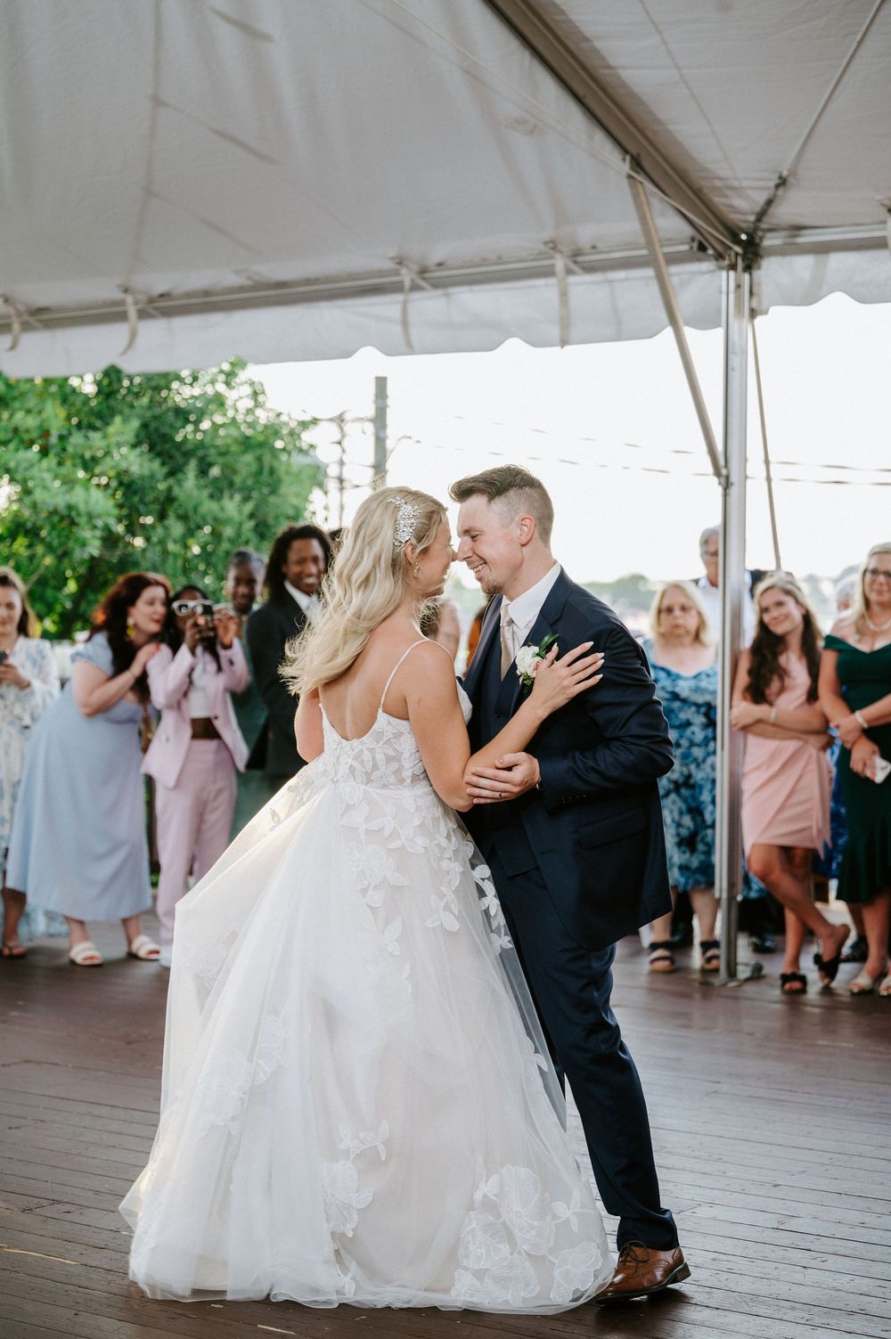 A couple shares their first dance under a white tent at an outdoor wedding reception.