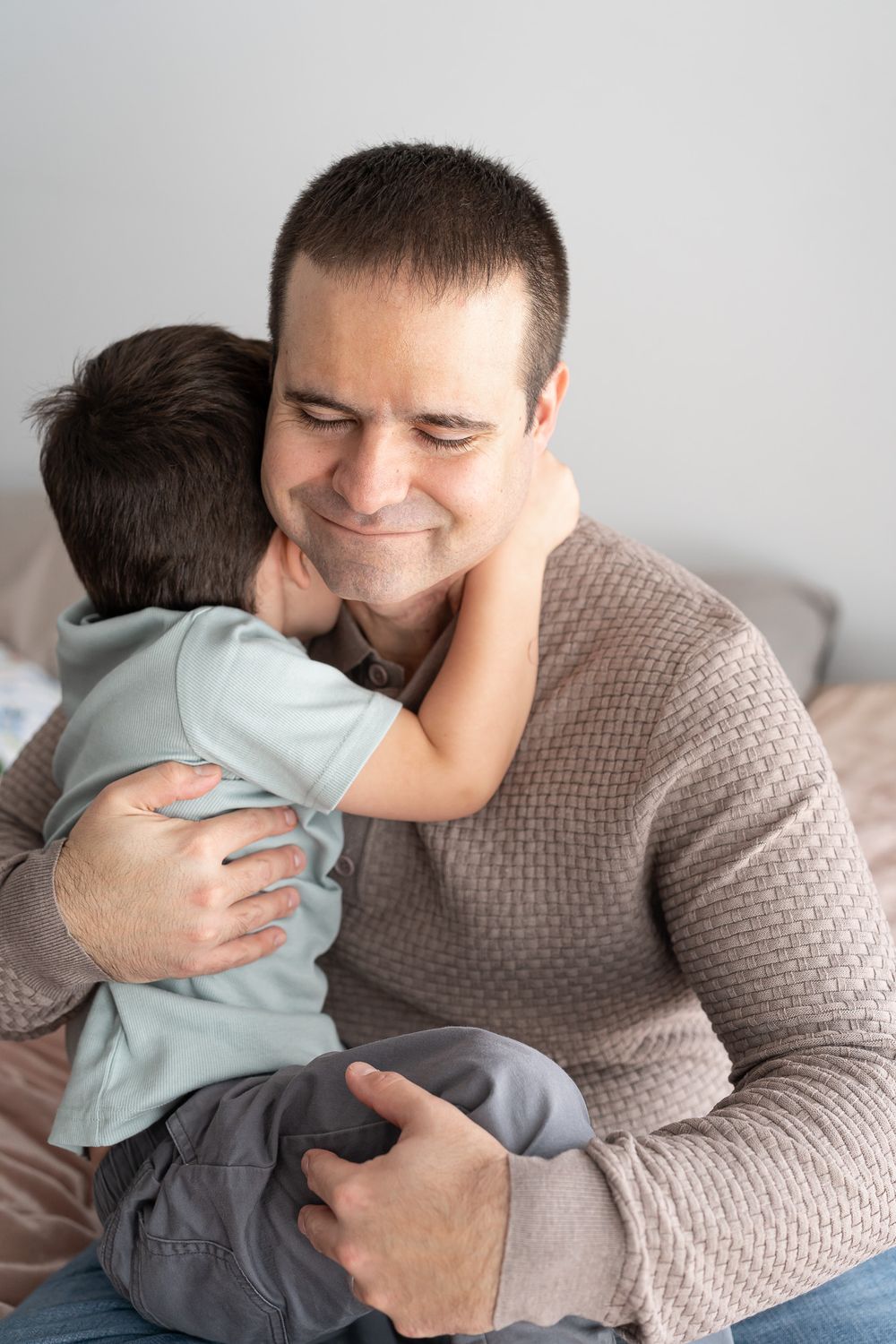 A parent in a beige sweater shares tender hugging moments with a child wearing light blue clothing.