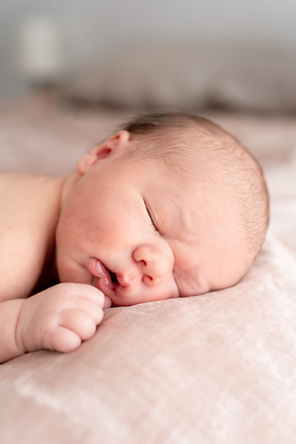 A peaceful sleeping newborn baby rests on soft pink bedding in natural light.