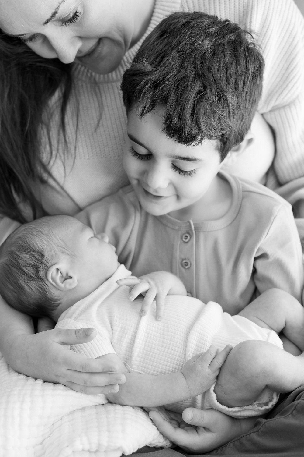 Black and white portrait of tender family moment with newborn baby and siblings.
