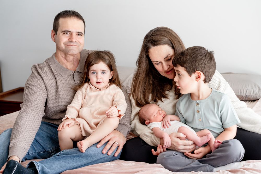 A family sits together on a couch sharing a tender moment with their newborn baby.