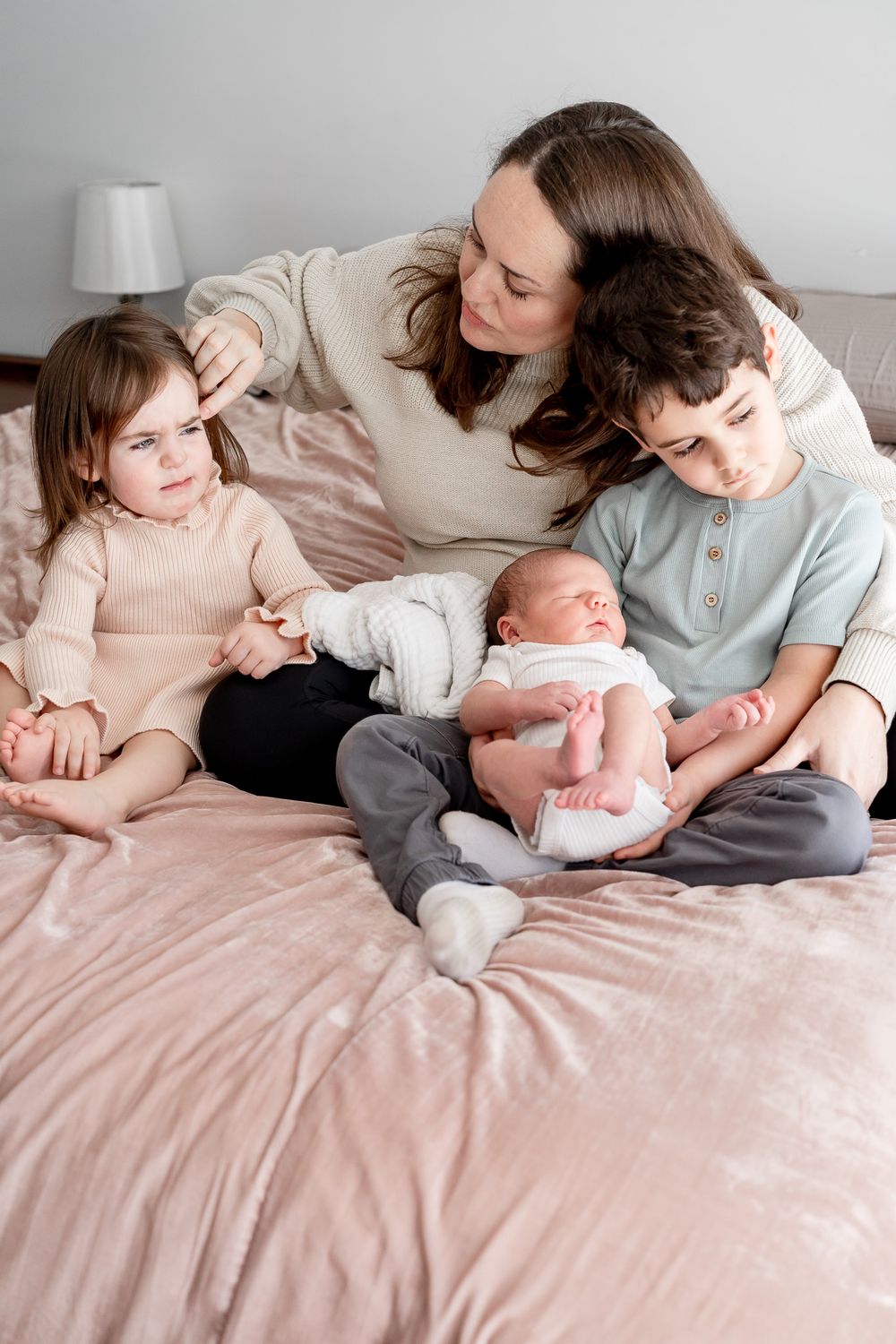 Family sitting together on pink bedding while holding and bonding with newborn baby.