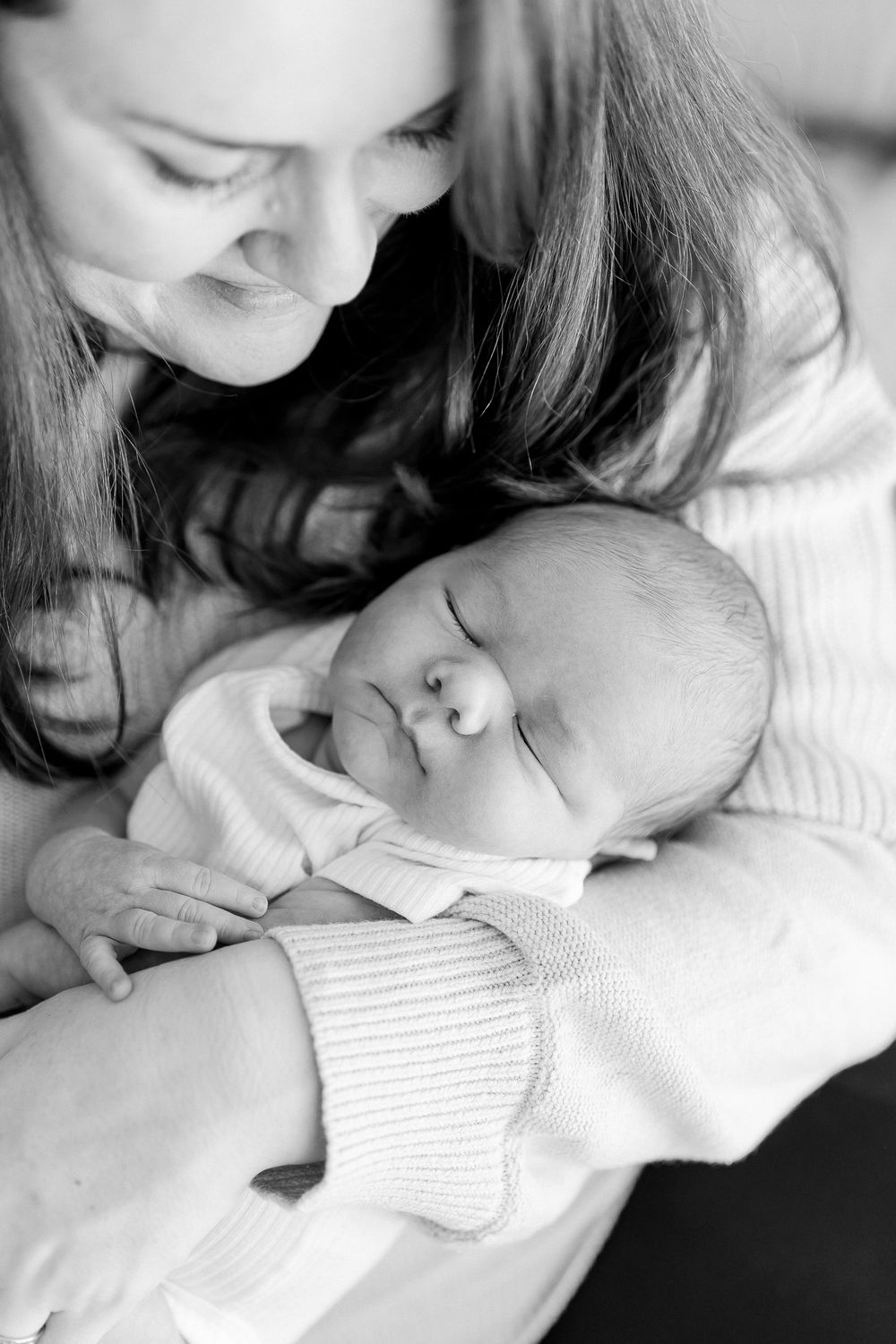 A tender black and white portrait of a sleeping baby in white clothing being held close.