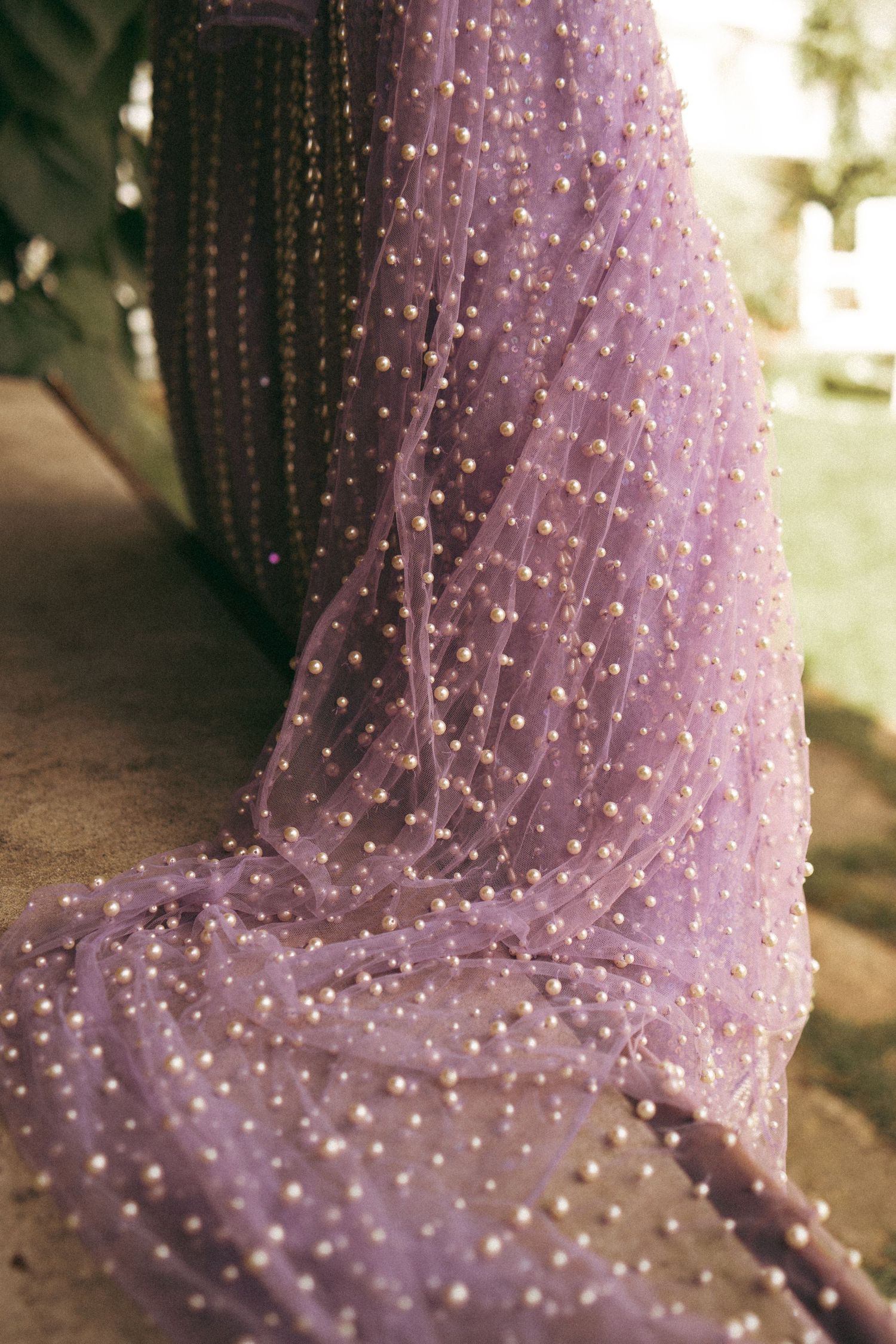 Elegant lavender tulle gown with pearl embellishments draped over a stone surface.