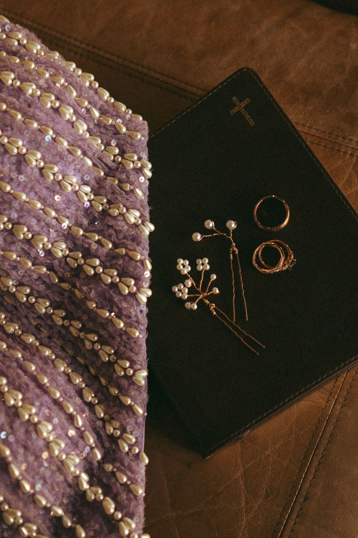 Purple beaded bridal fabric beside a black Bible with gold cross and pearl jewelry accessories.