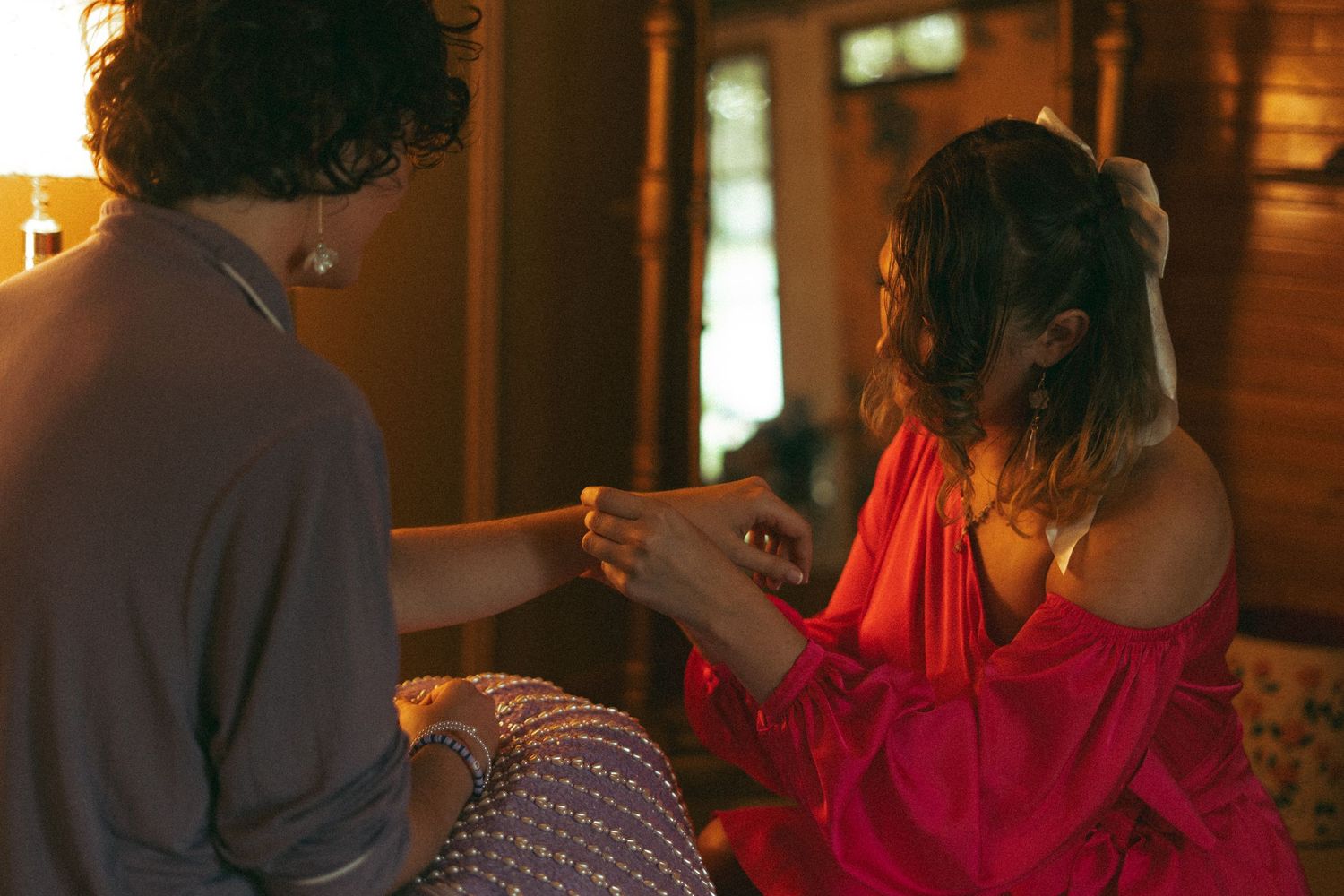 Woman in red dress placing a ring on a mans hand in a warmly lit room.