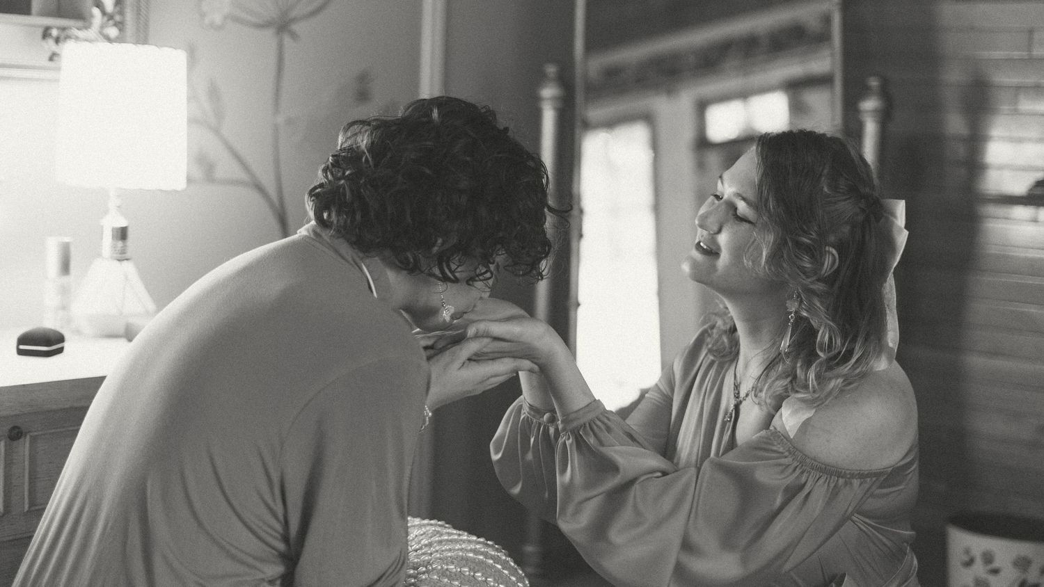 Black and white photo of a tender moment between a couple holding hands indoors.