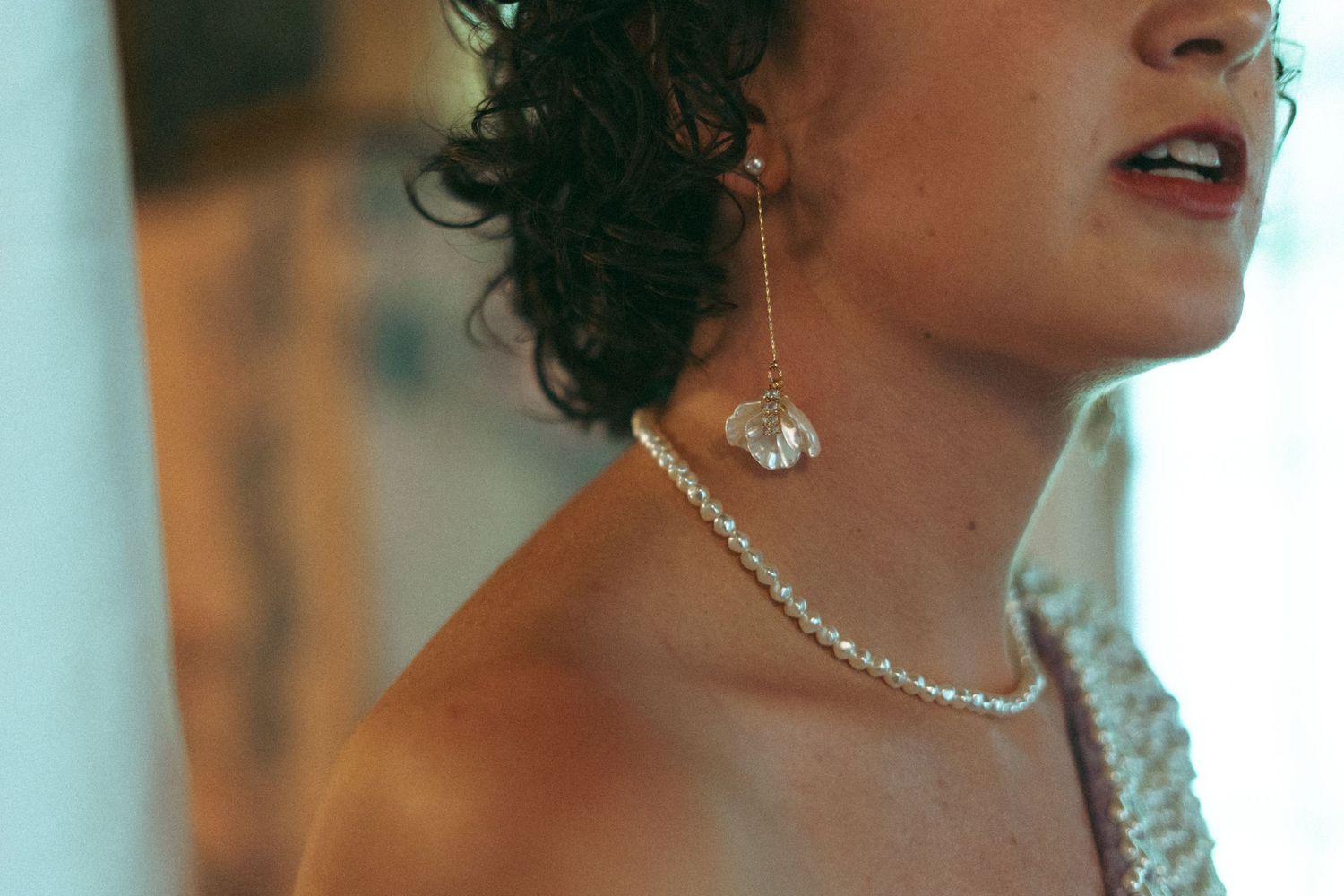 Close-up of a bride wearing pearl drop earrings and a delicate pearl necklace on her wedding day.