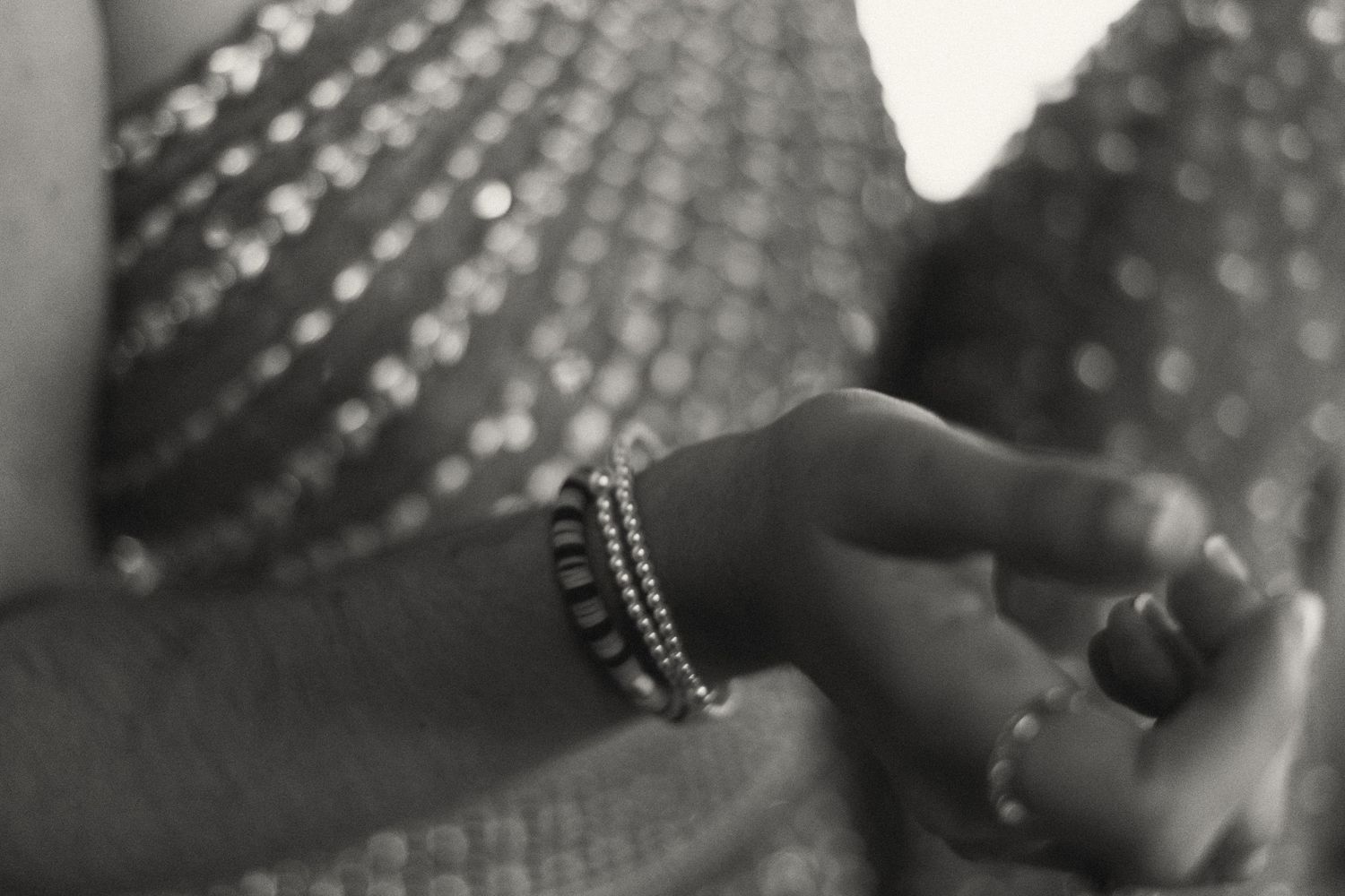 Black and white close-up of hands adorned with beaded bracelets holding fabric at a wedding.