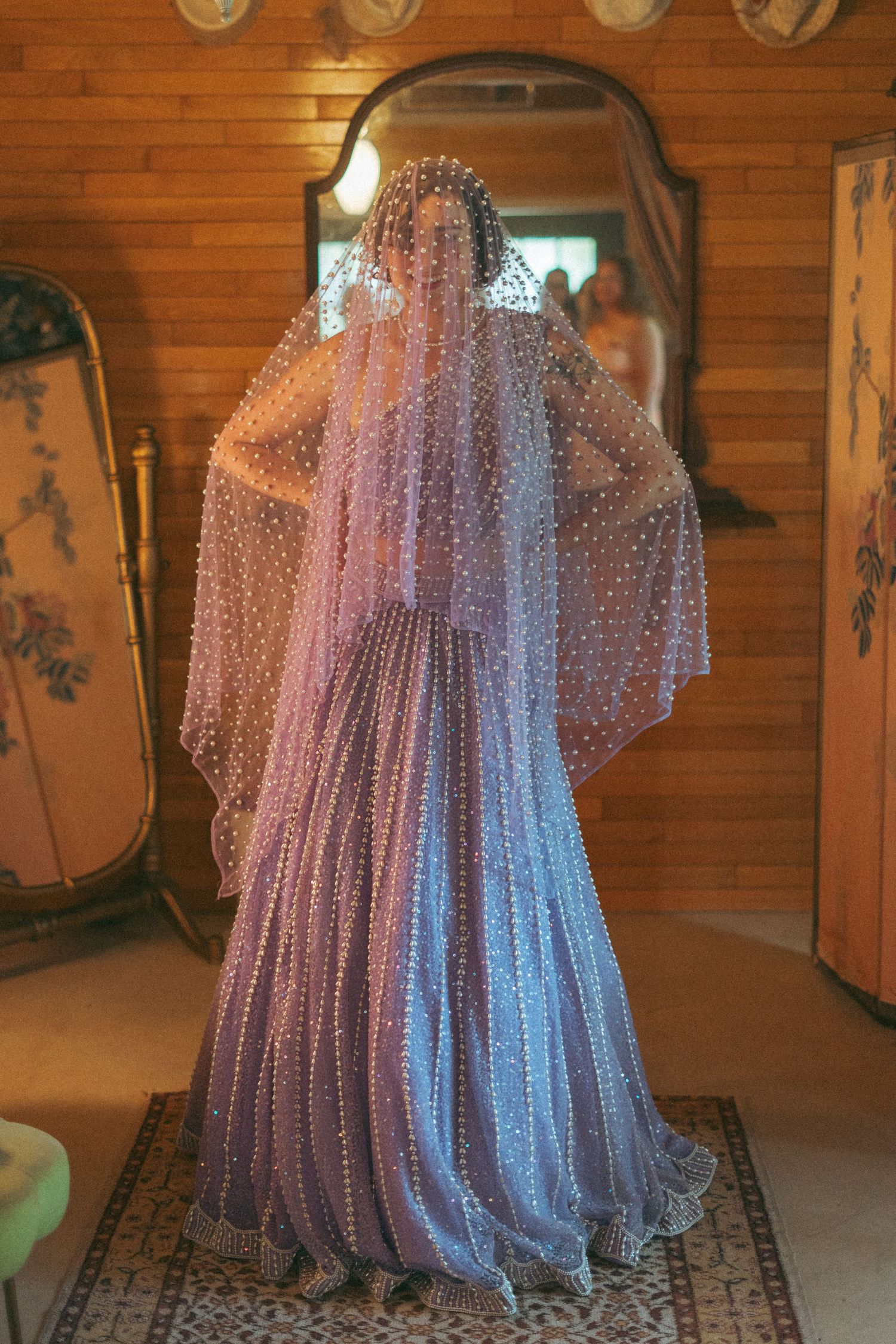 Bride wearing a stunning lavender pearl-embellished gown and matching veil in a vintage-styled room.