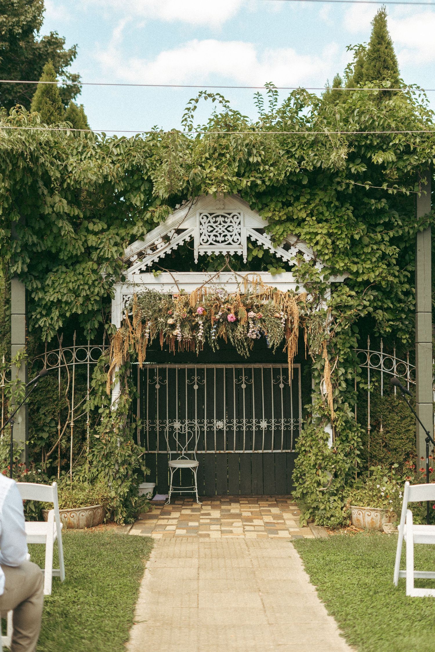 Ivy-covered garden gate adorned with dried flowers and greenery, serving as an outdoor wedding ceremony backdrop.
