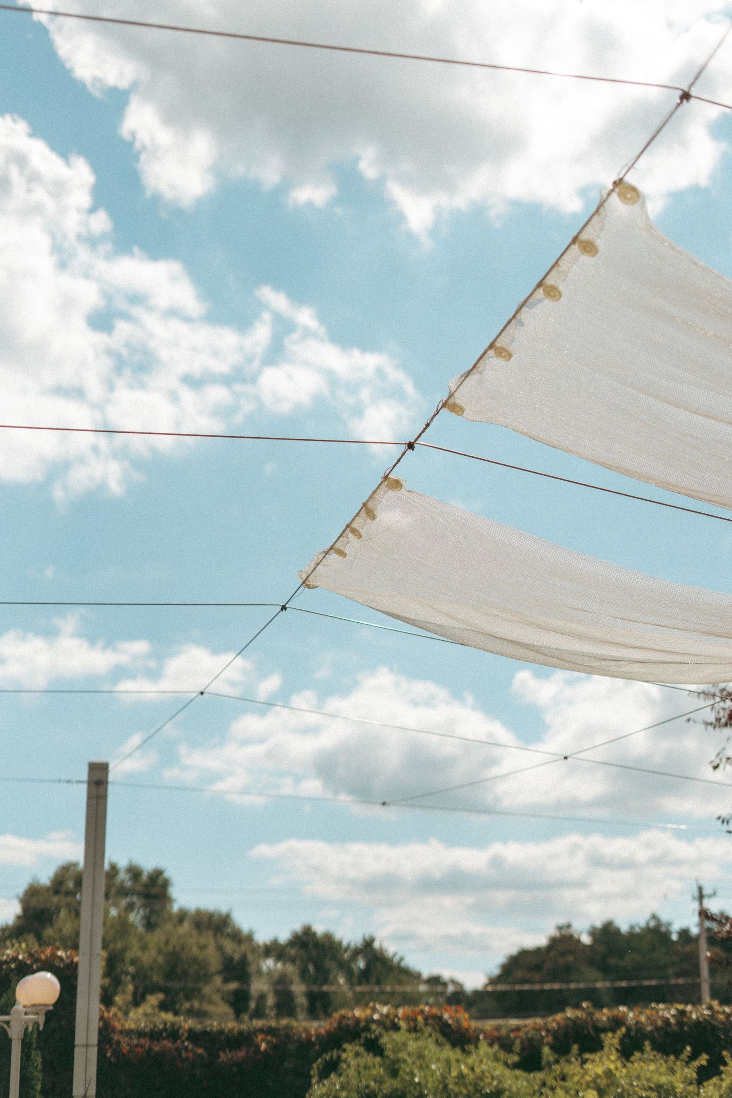 White fabric canopy panels with gold trim hanging against a bright blue sky at an outdoor wedding venue.