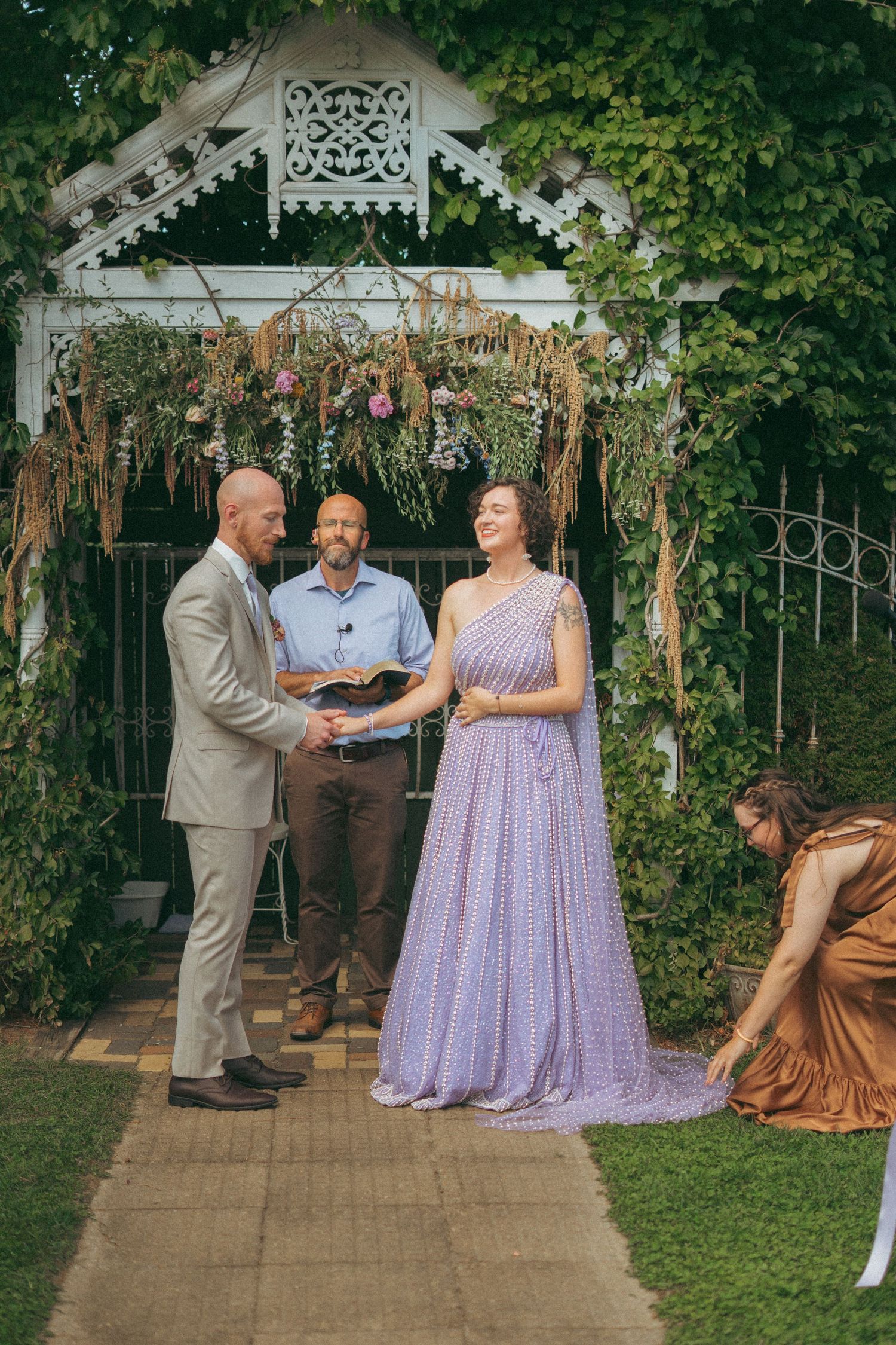 Couple exchanges vows in a purple wedding dress before an officiant at a garden wedding altar.