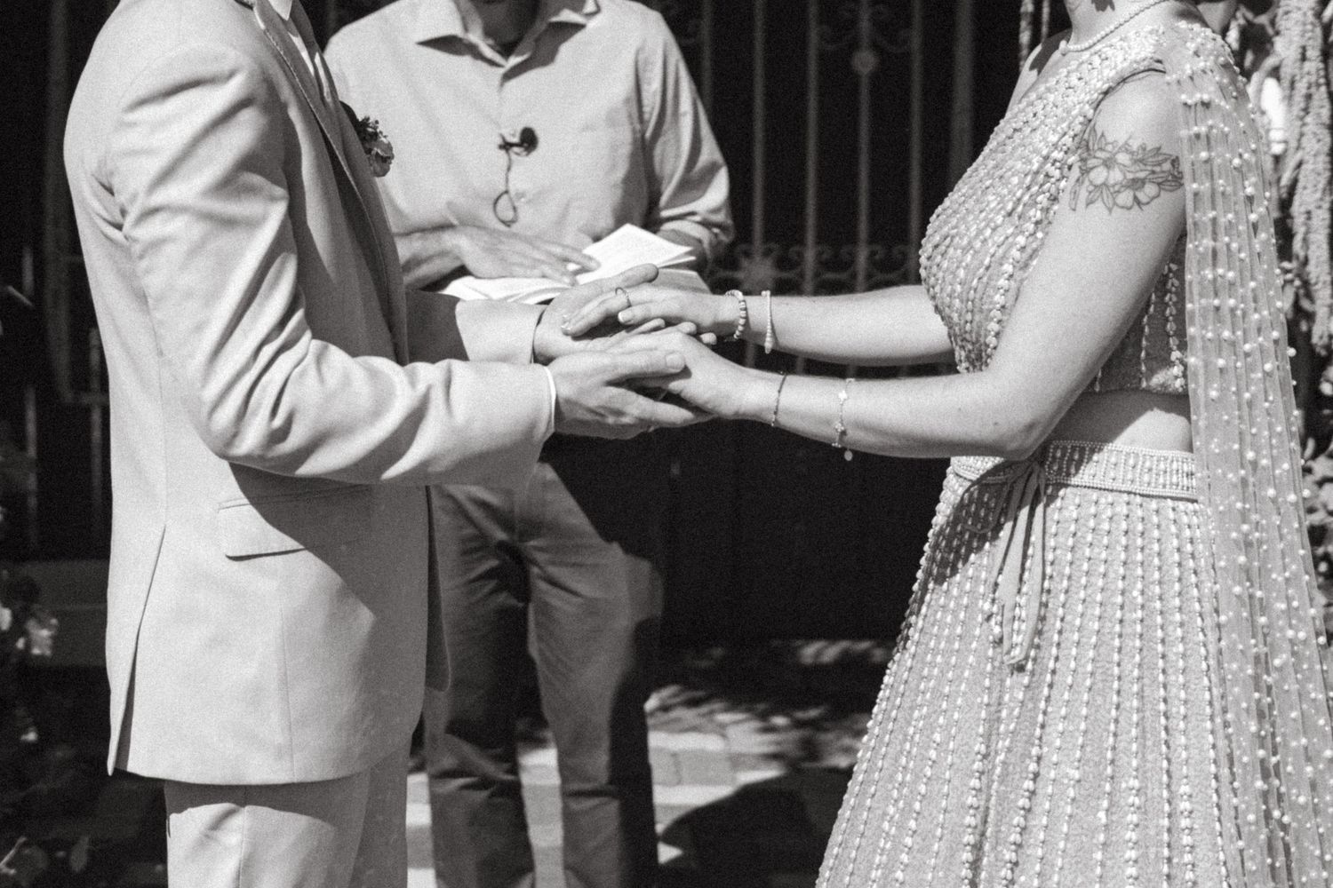 Black and white photo of couple holding hands during ring exchange with officiant at wedding.