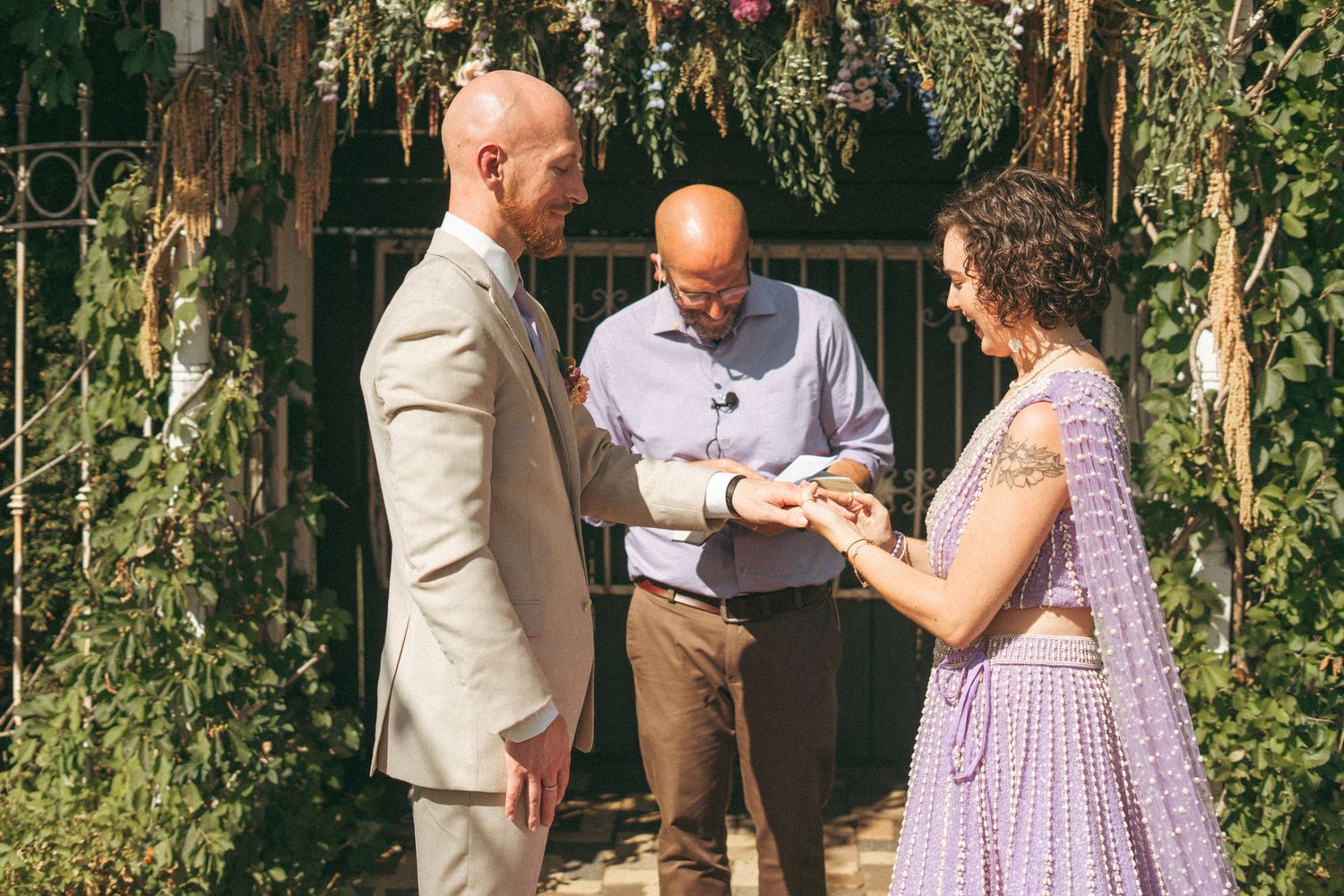 Couple exchanges rings during outdoor garden wedding ceremony with officiant holding a book.