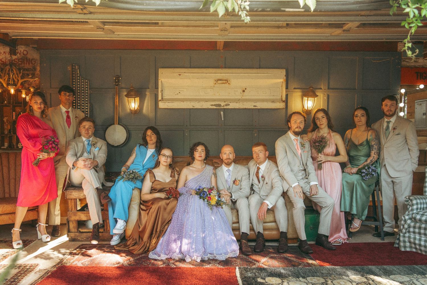 Wedding party group portrait seated and standing in eclectic venue, bride in lavender lehenga centerpiece.