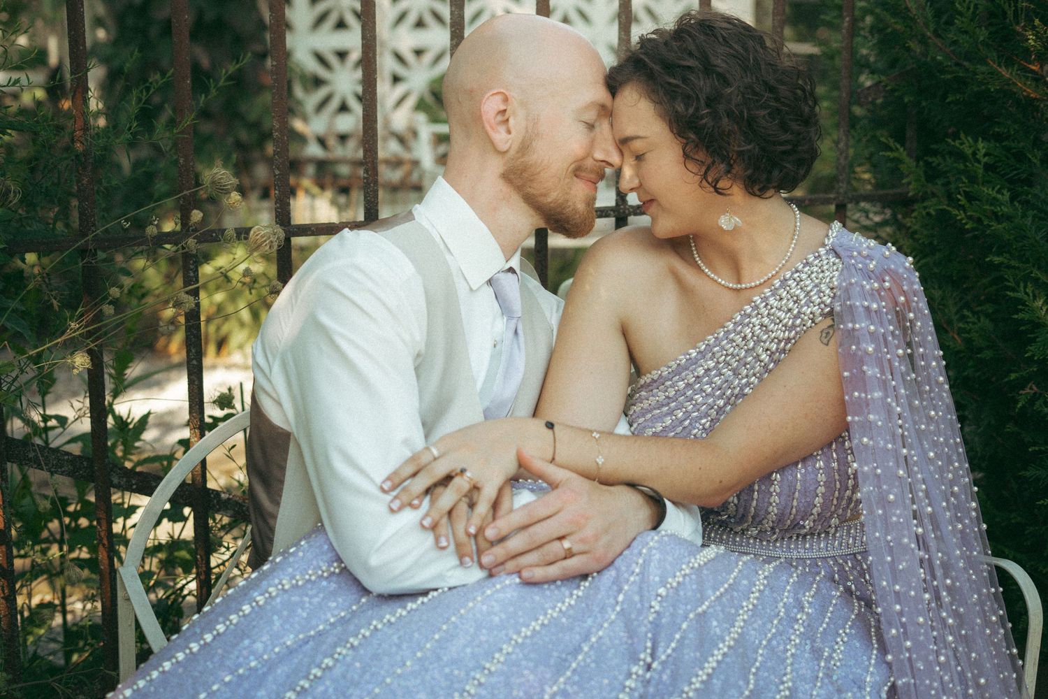 Bride and groom sharing intimate forehead touch moment seated outdoors, bride in beaded lavender lehenga.