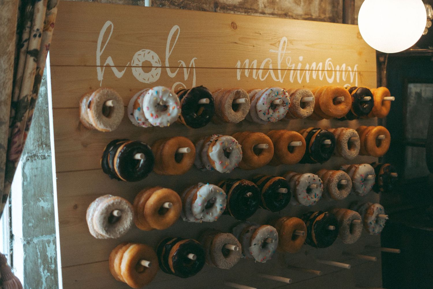 Rustic wooden donut wall display with assorted glazed donuts and holy matrimony calligraphy sign.