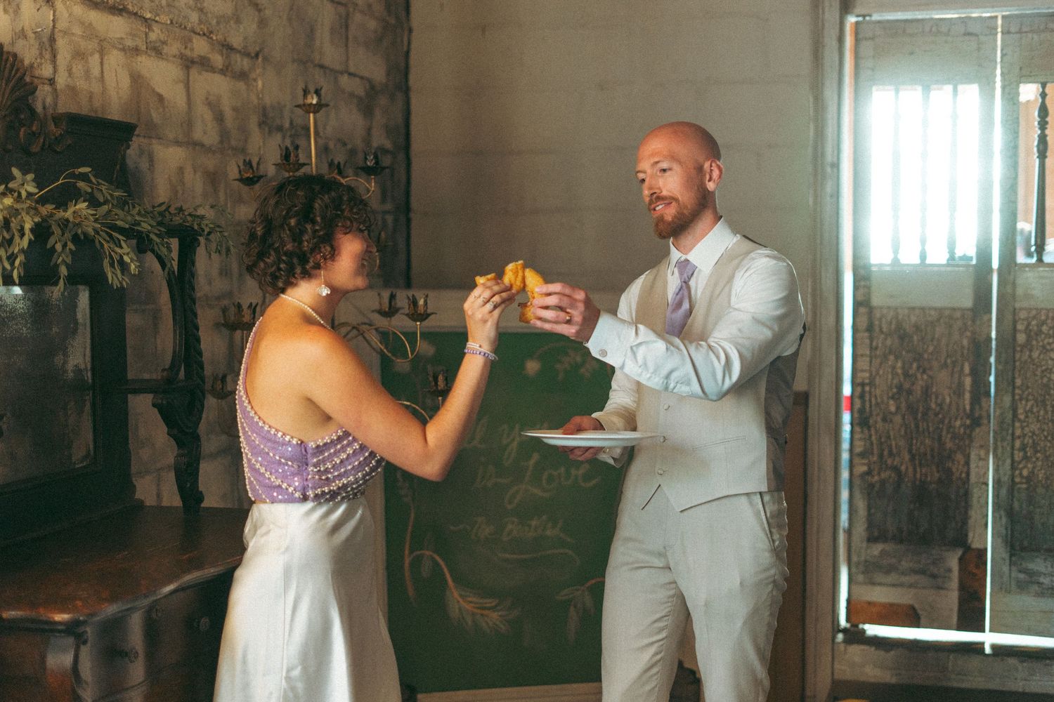 Bride and groom sharing food during their rustic wedding reception indoors.