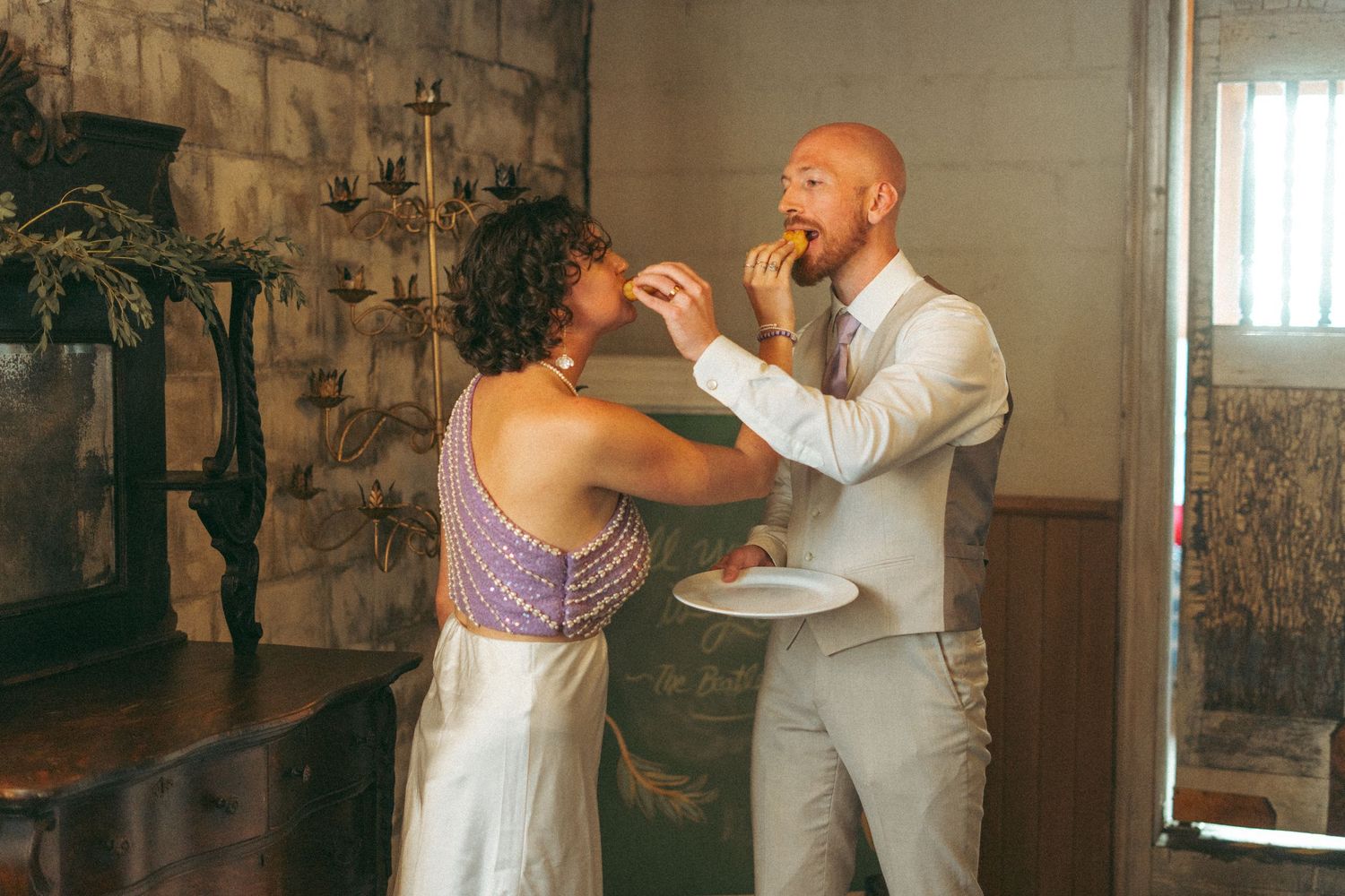 Bride feeding groom a bite of food during their wedding celebration in a stone venue.