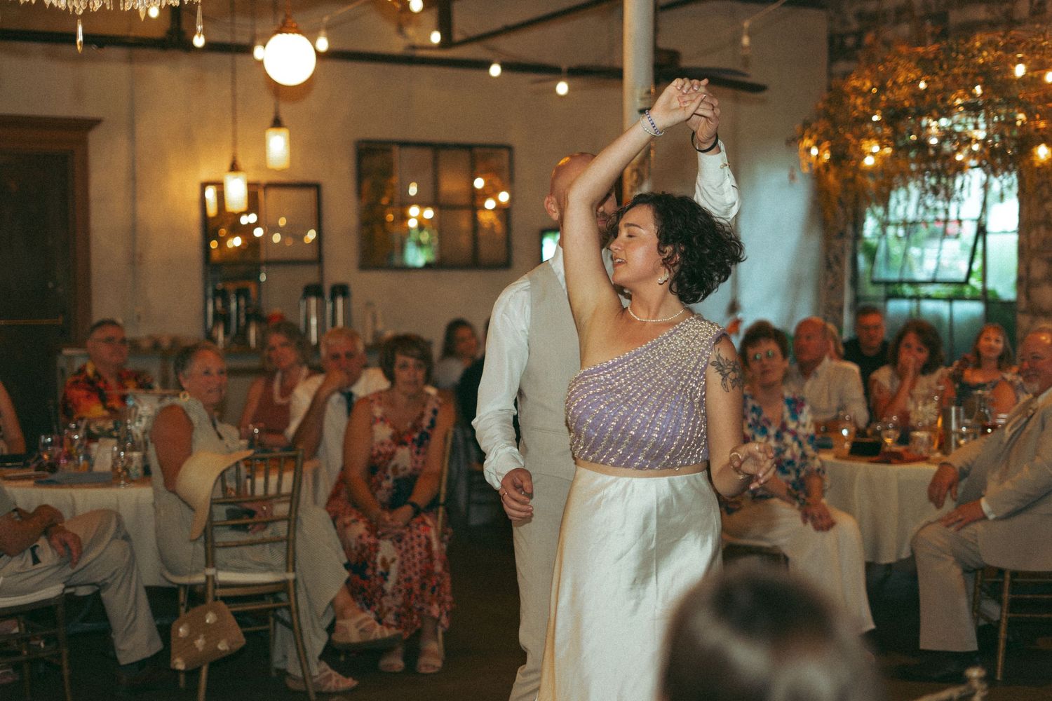 Bride and groom sharing their first dance under warm string lights at wedding reception.