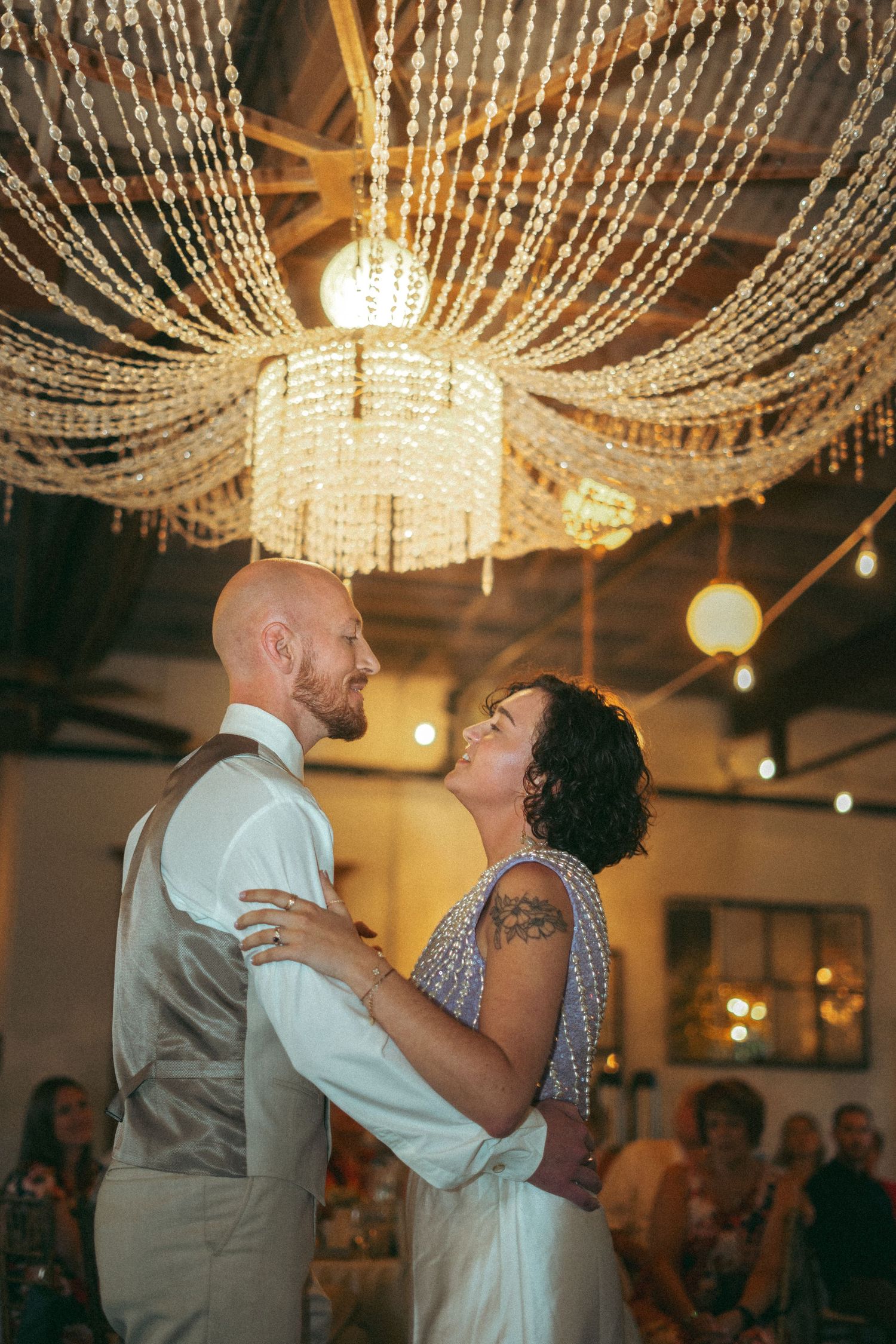 Couple sharing romantic first dance under a stunning crystal chandelier at wedding.