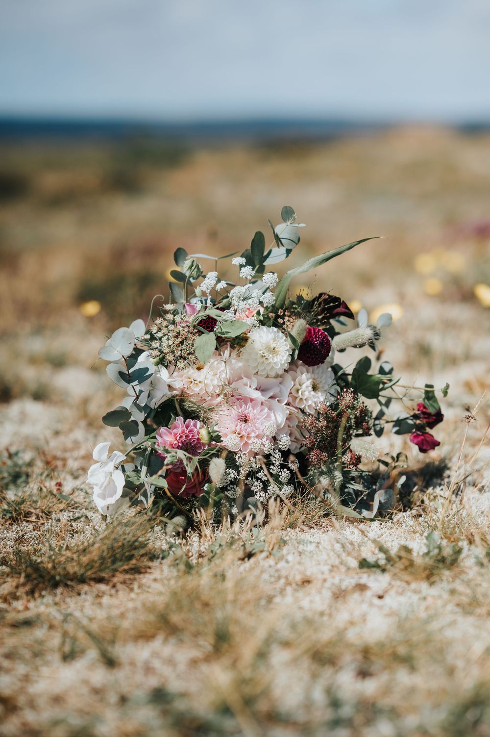 Delicate floral bouquet with pink roses and eucalyptus leaves arranged artistically on textured sandy ground.