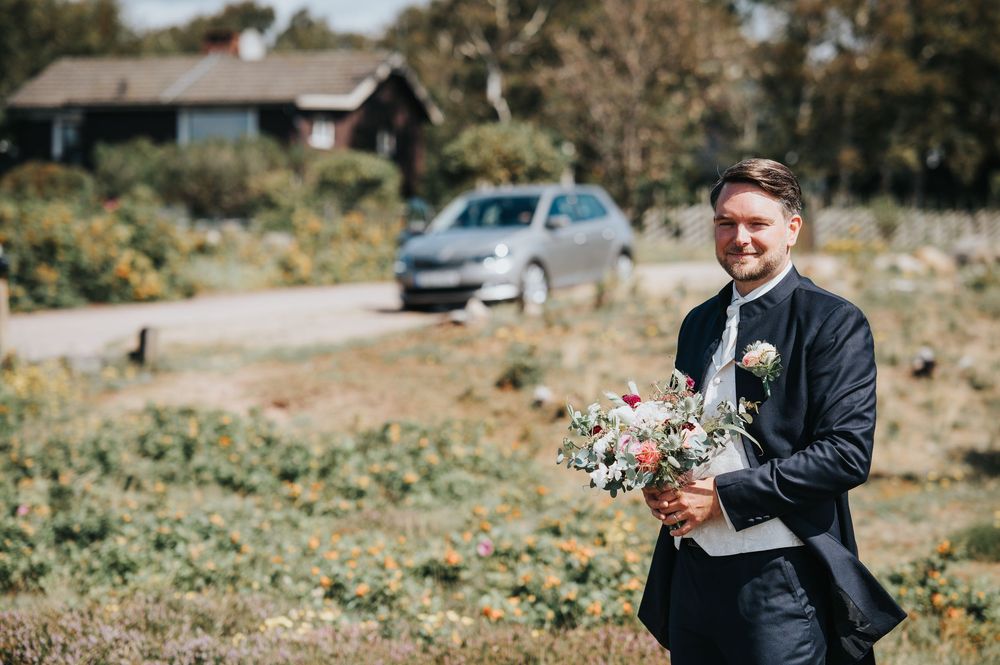 A person in a black suit and tie holds a small furry puppy outdoors on a sunny autumn day.