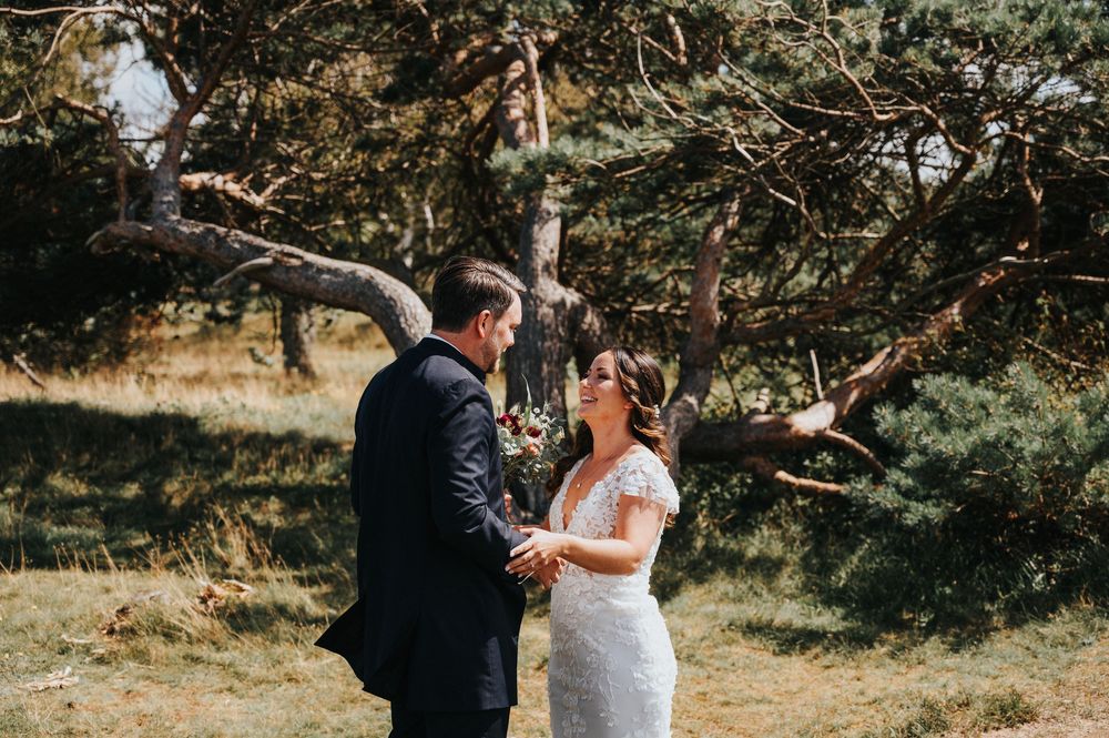 A couple shares an intimate moment during their outdoor wedding ceremony in a sunlit forest setting.