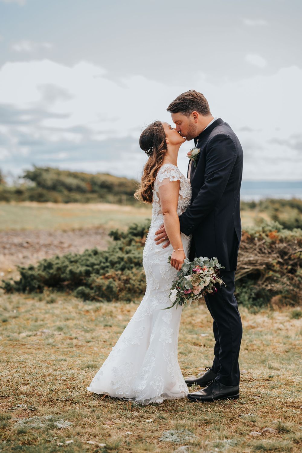 Romantic wedding couple shares intimate moments on a coastal hillside with natural scenery in the background.
