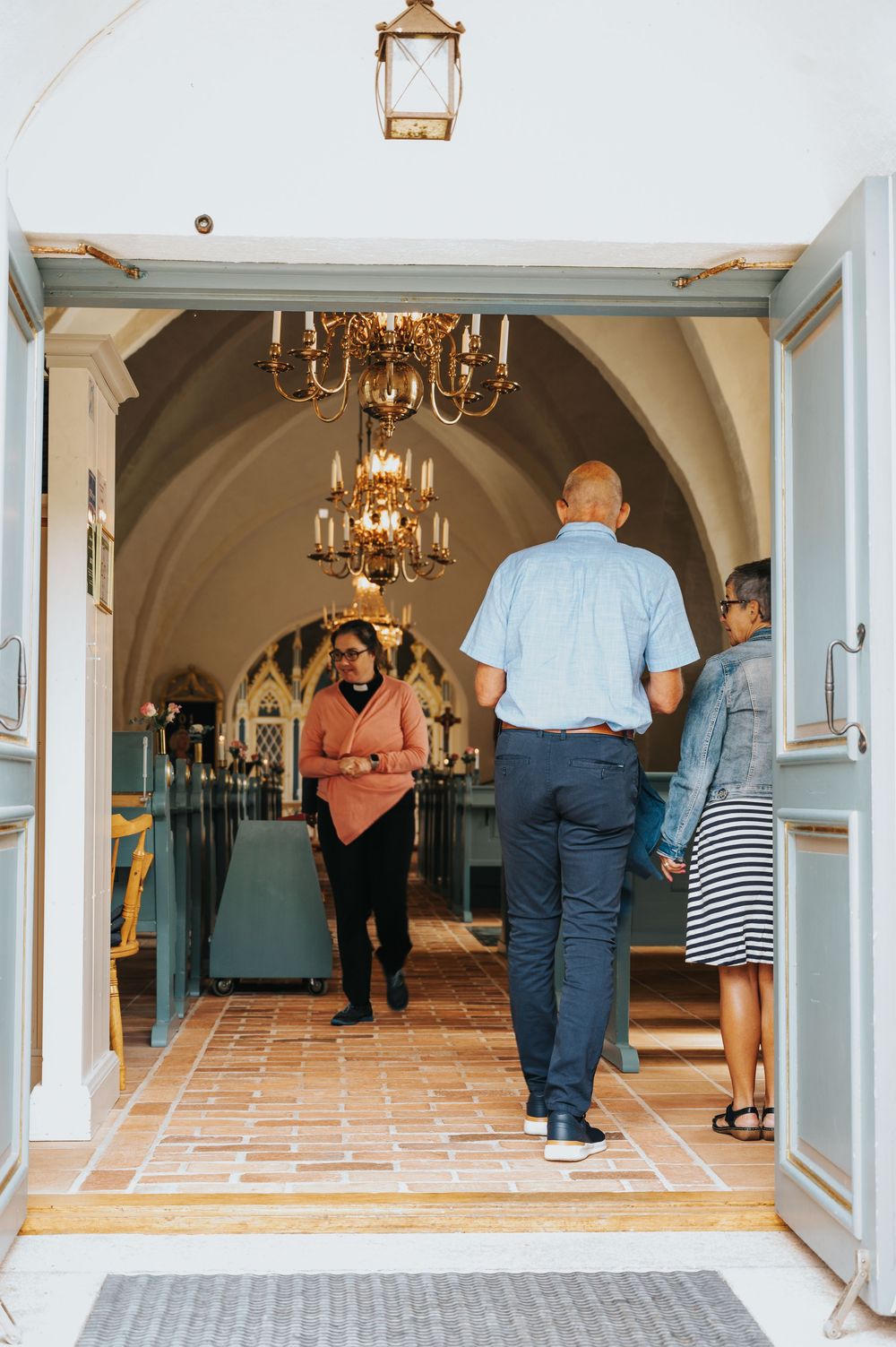 An elegant church hallway with arched ceilings, chandeliers, and terracotta flooring.