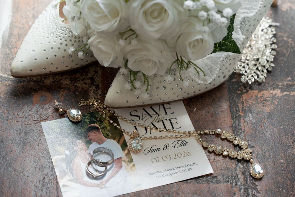 White roses and wedding accessories including pearls, invitation cards, and bridal shoes arranged on a rustic surface.