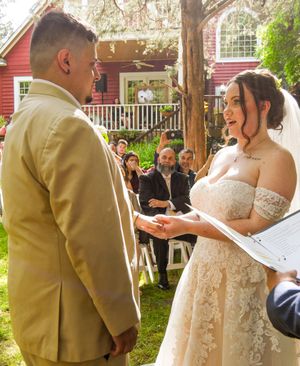 A bride and groom exchange vows during an outdoor wedding ceremony under a wooden pergola.