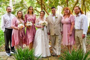 Wedding party in pink dresses and khaki suits poses outdoors in a garden setting.