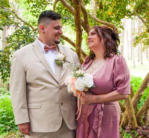 A couple in coordinated beige and mauve outfits share romantic moments in a lush garden setting during a photo session.