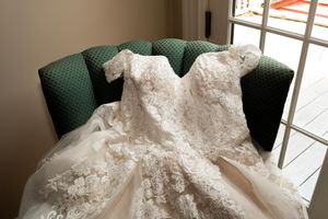 White lace wedding dress displayed in natural light against a window with plantation shutters.