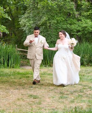 Playful wedding couple dancing and twirling in a garden setting with lush green foliage.