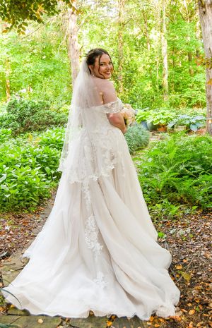 Two wedding gowns with flowing white trains twirl together in a lush forest setting.