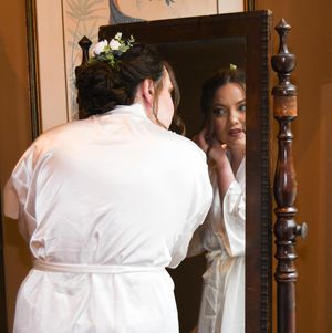 Person in white robe looking in mirror while getting ready in elegant bathroom interior.