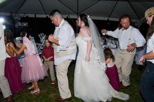 Wedding reception guests dance under a tent at an outdoor evening celebration.