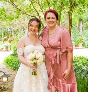 Bridal party in dusty rose dresses and white gown pose together in a lush garden setting.