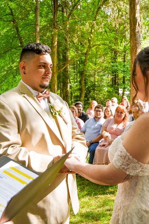 A couple shares their first dance together in a sun-dappled forest setting surrounded by wedding guests.