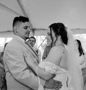 A black and white wedding photo captures a tender moment between newlyweds dancing under a tent.