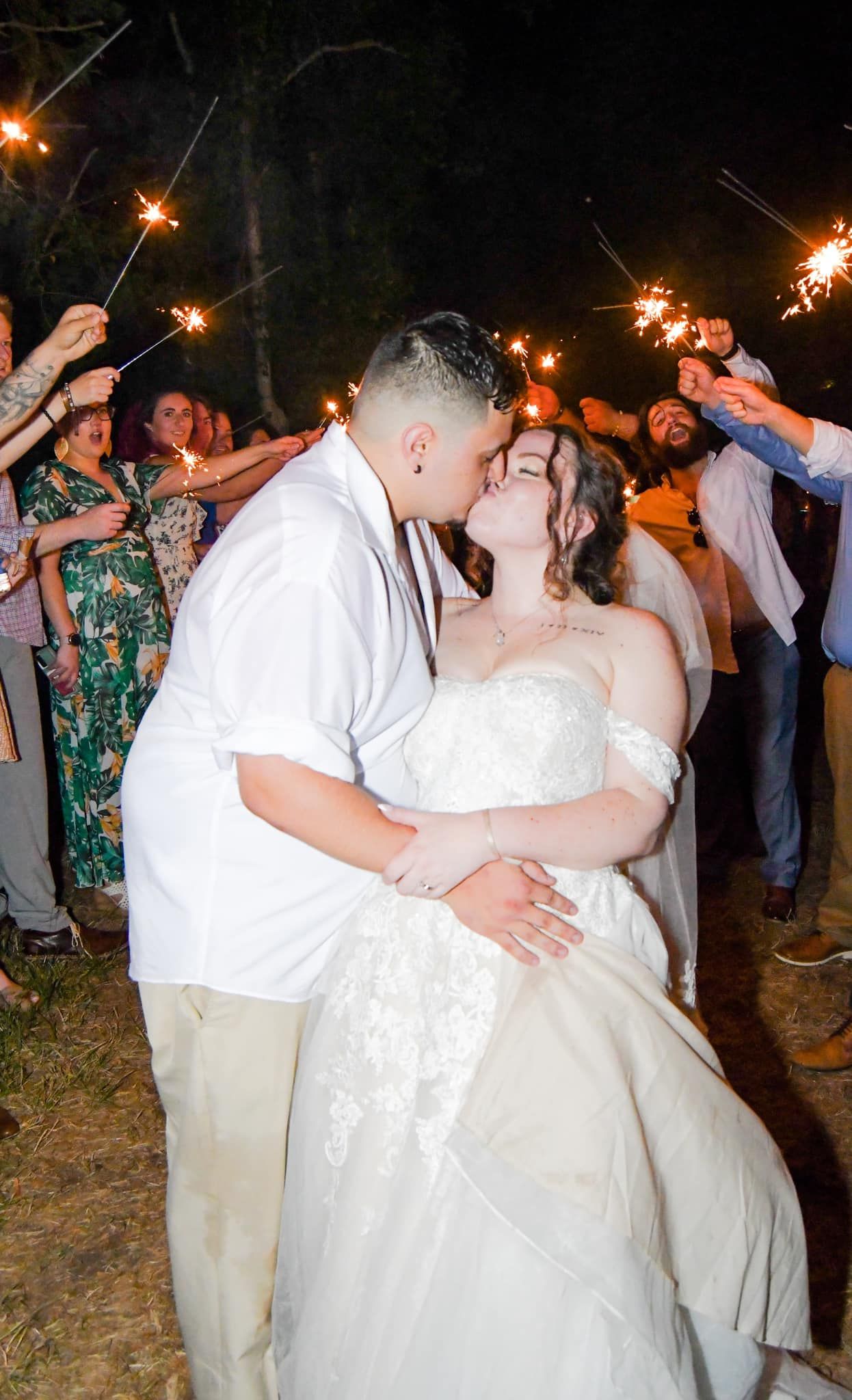 A couple shares their first dance under sparklers at an outdoor evening wedding celebration.